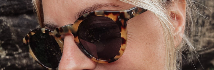 Woman wearing tortoiseshell sunglasses with a blurred natural background